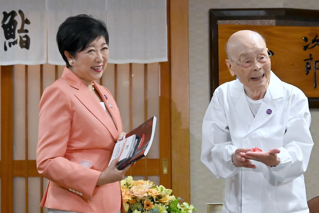 Jiro Ono (right) shows a gift from Tokyo Governor Yuriko Koike to celebrate his 100th birthday in front of  Sukiyabashi Jiro on September 18. Photo: Bureau of Social Welfare, Tokyo Metropolitan Government/AP