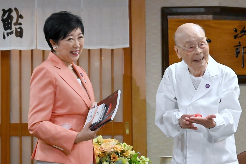 Jiro Ono (right) shows a gift from Tokyo Governor Yuriko Koike to celebrate his 100th birthday in front of Sukiyabashi Jiro on September 18. Photo: Bureau of Social Welfare, Tokyo Metropolitan Government/AP