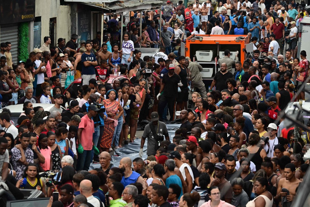Residents stand next to bodies lined up in front of a morgue truck on Sao Lucas Square, Vila Cruzeiro favela, in Rio de Janeiro. Photo: AFP