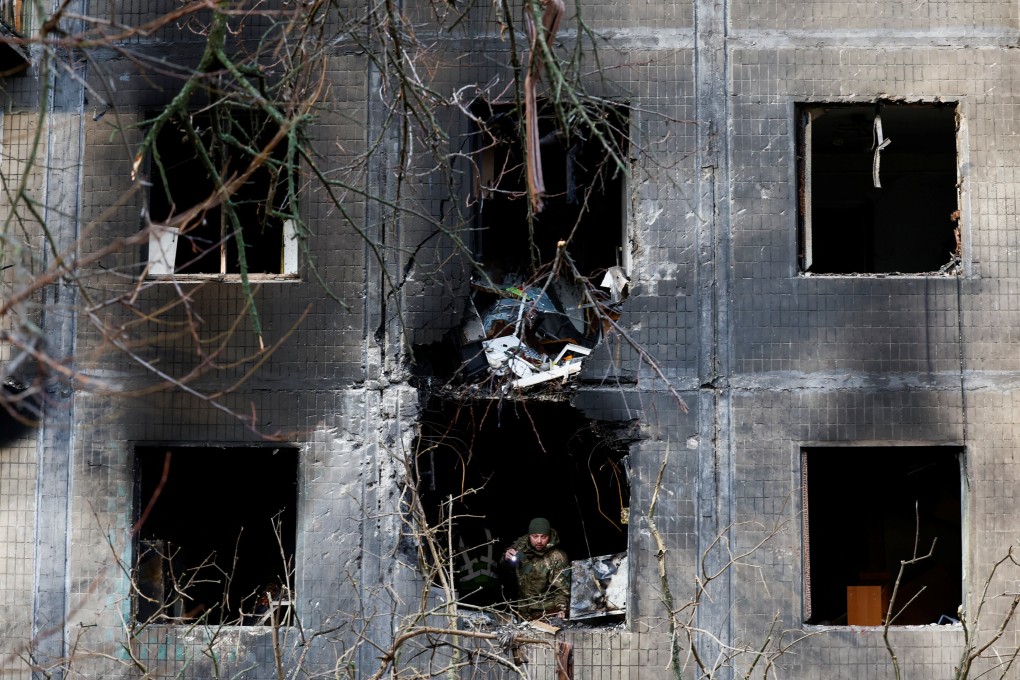 An investigator looks through the window of a Kyiv residential building after an overnight Russian drone and missile strike. Photo: Reuters