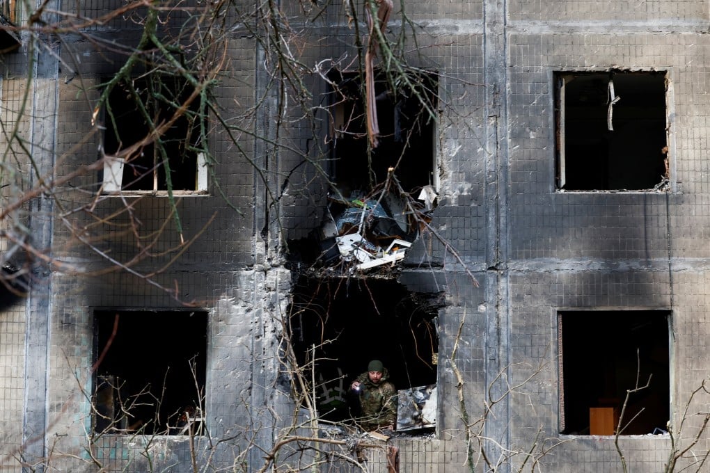An investigator looks through the window of a Kyiv residential building after an overnight Russian drone and missile strike. Photo: Reuters