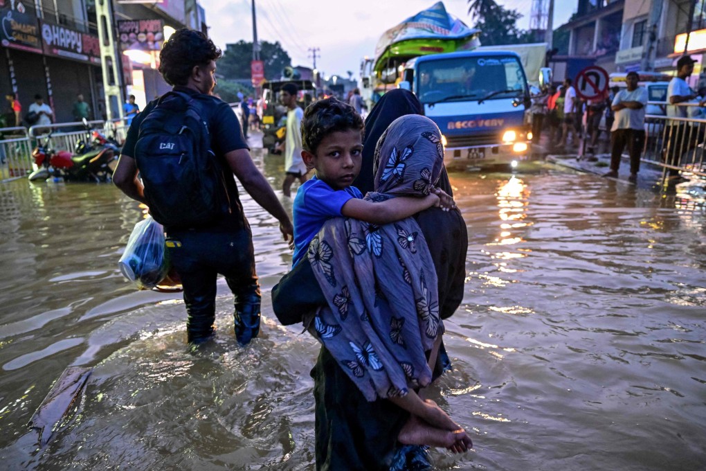 A woman carries a child as she wades through a flooded street after heavy rainfall in Wellampitiya, Sri Lanka, on November 30. Photo: AFP