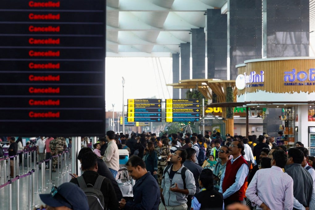 Travellers look at updates on flights, as they stand next to a screen displaying details of cancelled IndiGo airlines flights, at Kempegowda International Airport in Bengaluru, India, on Saturday. Photo: Reuters