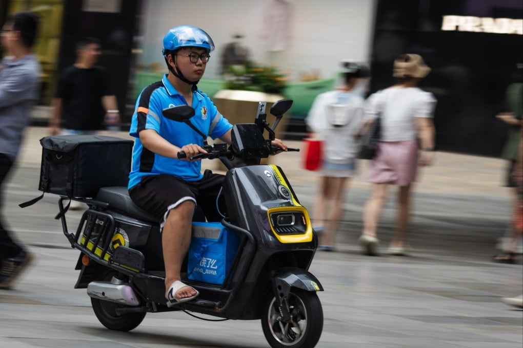 A food delivery rider from Ele.me, wearing a blue helmet and uniform, rides an electric scooter through a busy commercial pedestrian street on July 20 in Chongqing, China. Photo: Getty Images