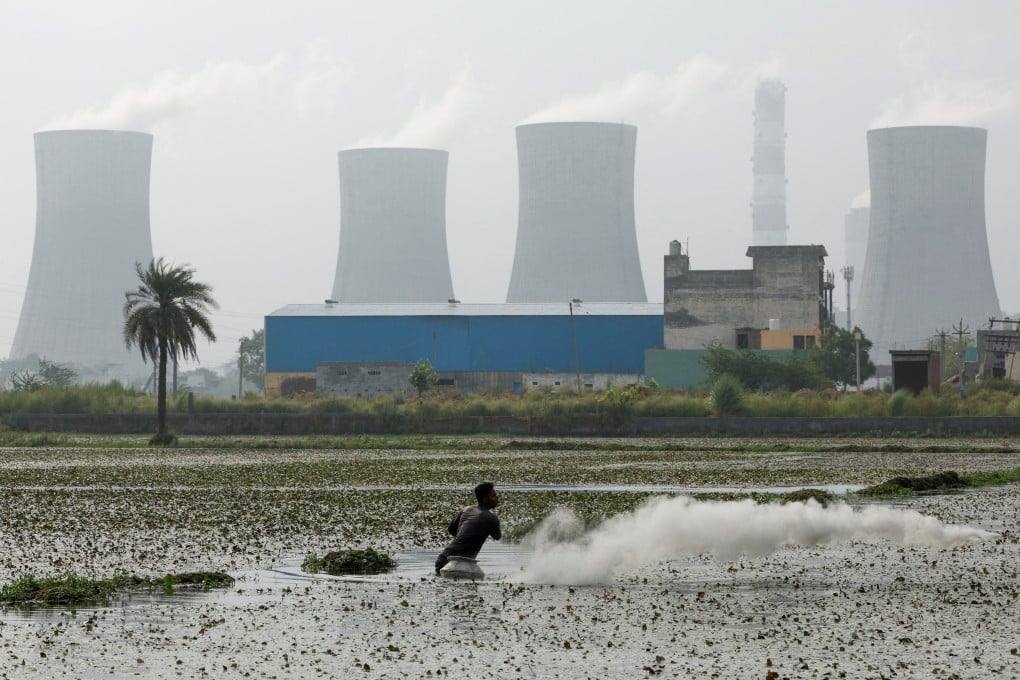 An Indian farmer sprinkles pesticide on a field as smoke rises from the chimneys of a coal power plant. The demand for coal-based power plants has risen due to prolonged heatwaves. File photo: Reuters