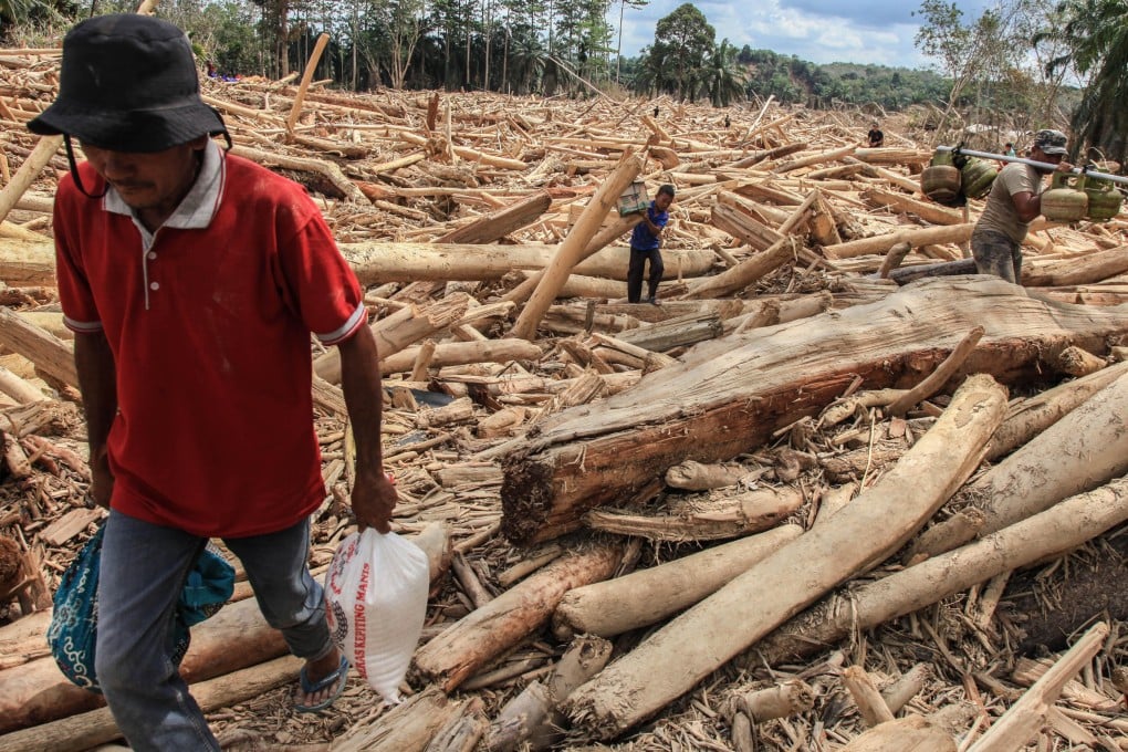 People carry their belongings as they walk on logs swept away by a flash flood in Aceh Tamiang on Monday. Photo: EPA