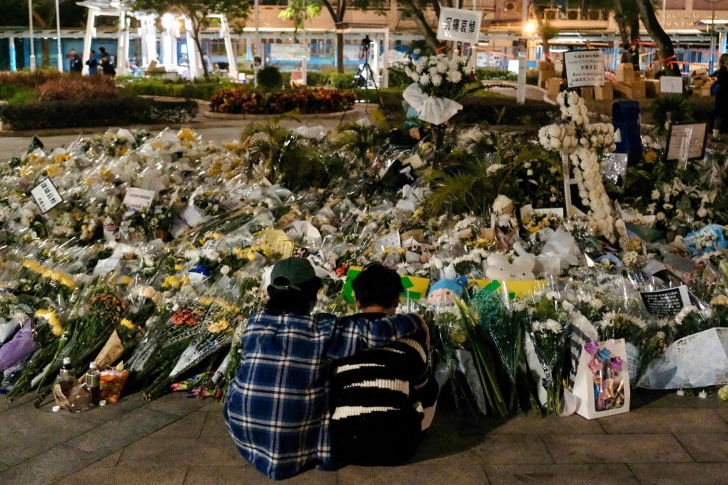 Volunteers take a moment on December 8, in front of flowers left by mourners for the victims of the Tai Po fire tragedy. Photo: AFP