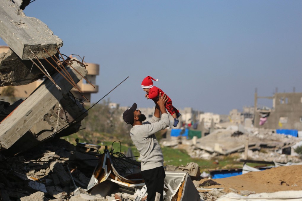 A Palestinian man lifts a baby next to the rubble of destroyed buildings in Gaza on Christmas Eve. Photo: AFP