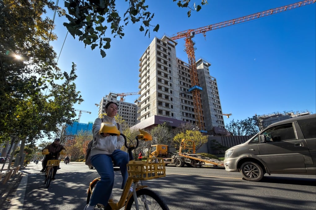 A woman rides past a residential construction site where cranes stand above an unfinished apartment building, in Beijing. China’s property sector has been mired in a downturn since 2021. Photo: Getty Images