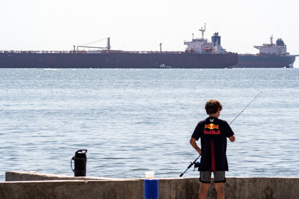 A boy fishes in front of oil tankers anchored near Maracaibo, Venezuela, in December. Photo: TNS