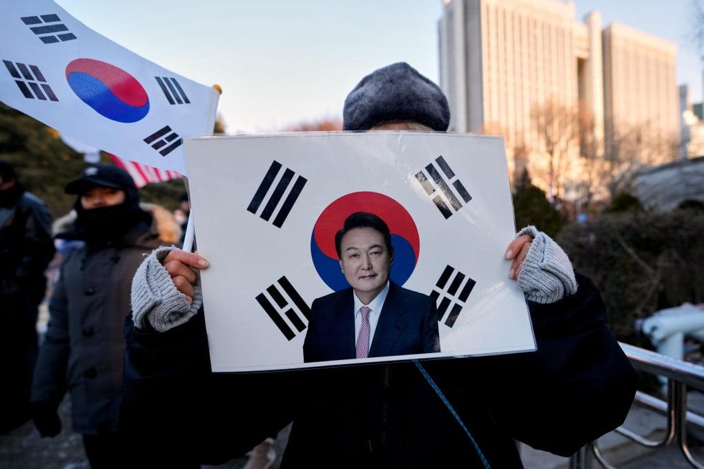 Outside a district court in Seoul, South Korea on Tuesday, a supporter of former President Yoon Suk-yeol holds a sign bearing his image and a flag. Photo: AP