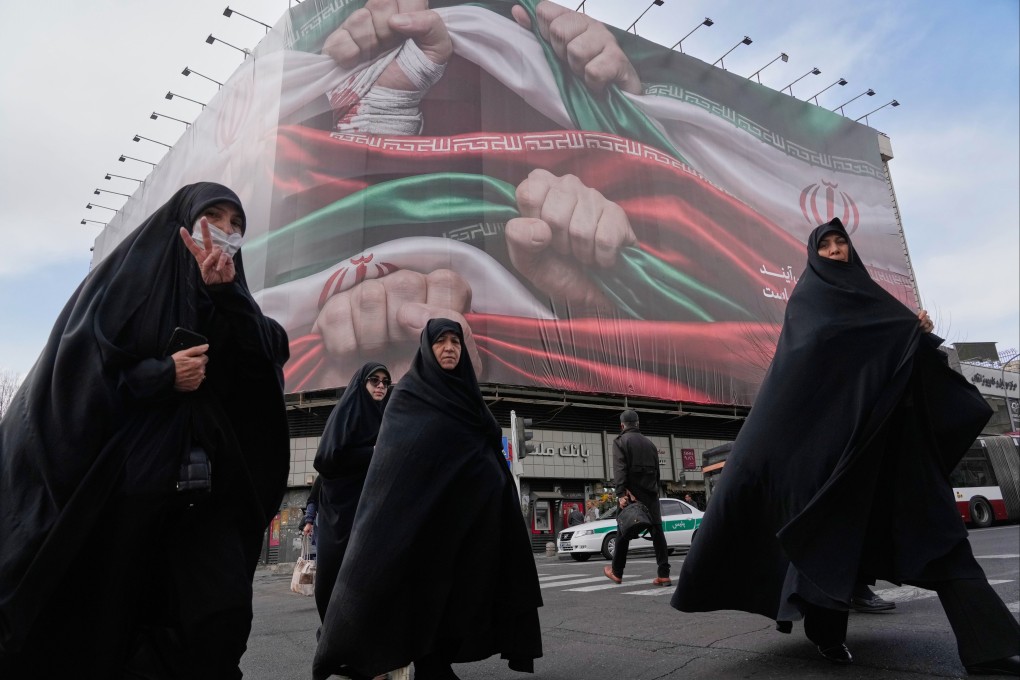 Women cross a street under a huge banner showing hands firmly holding Iranian flags in Tehran on Wednesday. Photo: AP