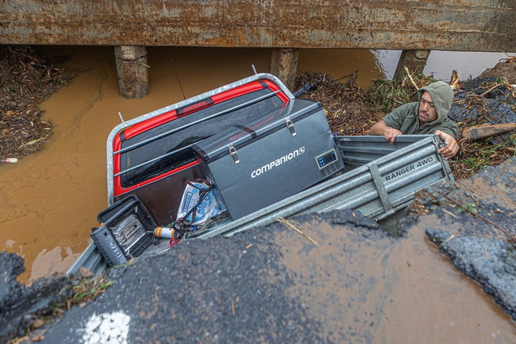 A man retrieves his belongings from a utility vehicle that plunged off a collapsed section of road in Puketotara, New Zealand, on Saturday. Photo: Wayne Feisst via Reuters
