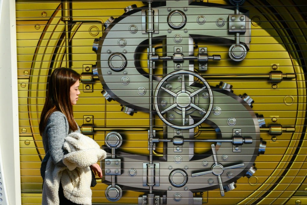A pedestrian passes in front of a currency mural on a shop’s gate in Hong Kong. Photo: Antony Dickson