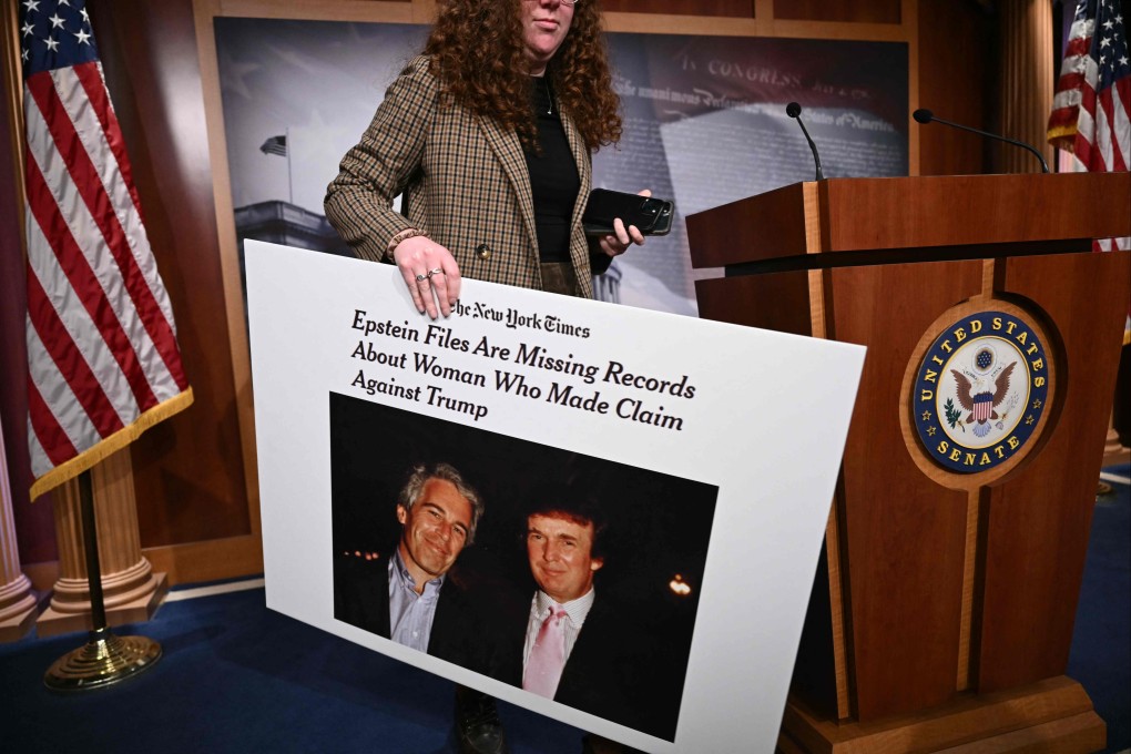 A staff member holds a sign showing a photo of Jeffrey Epstein and Donald Trump after a press conference with US Senate Minority Leader Chuck Schumer on February 26. Photo: AFP