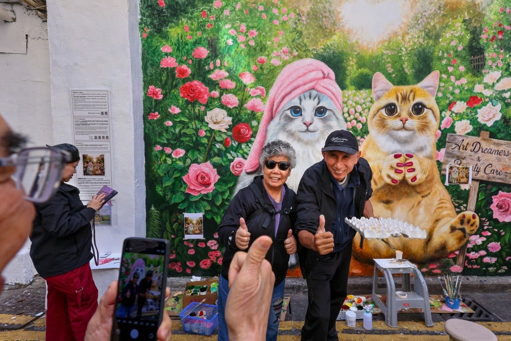 Artist Li Hok-fung (right) takes a photo with a resident in front of his popular cat-themed mural at Kiu Kong Mansion in Yau Ma Tei. Photo: Dickson Lee