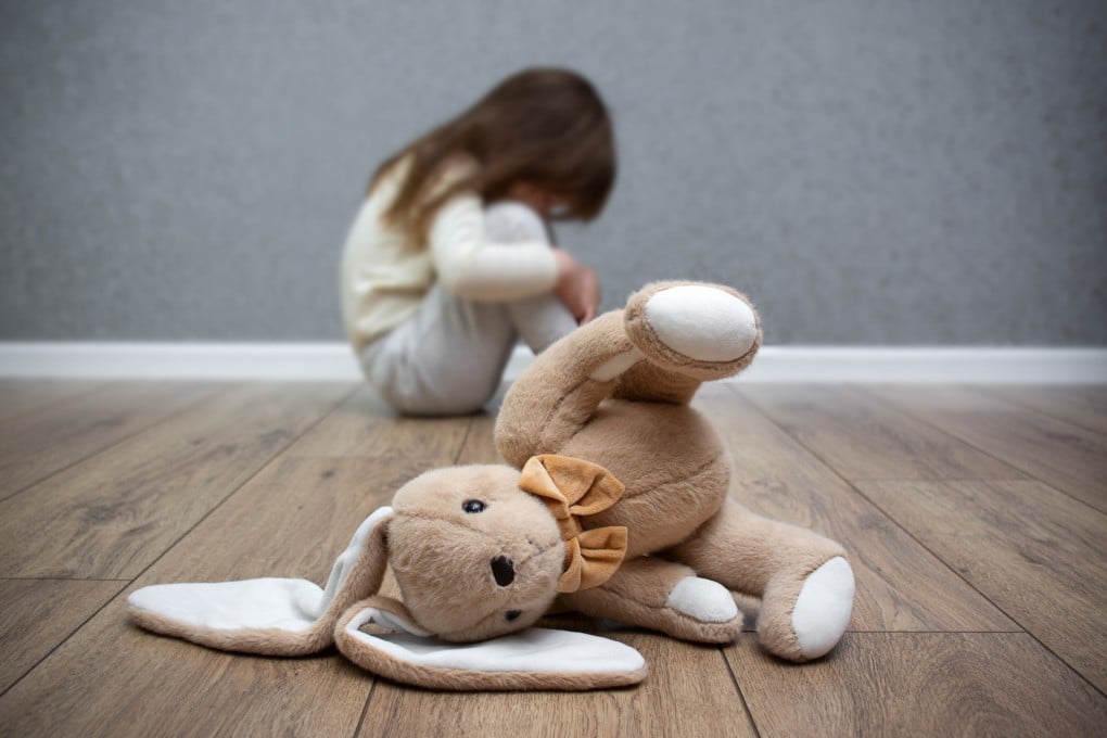 A stuffed bunny on the floor, a scared child sitting behind it. Child abuse. Bullying in the family. Photo: Getty Images