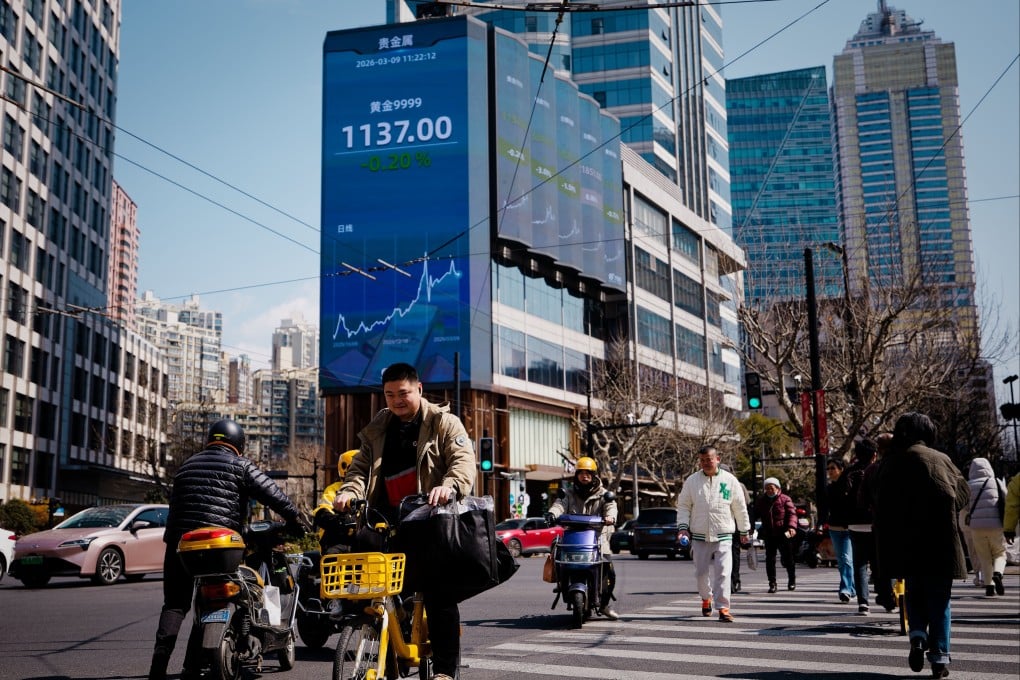 People cross the street beneath a large screen showing stock data in Shanghai on March 9, 2026. Photo: EPA