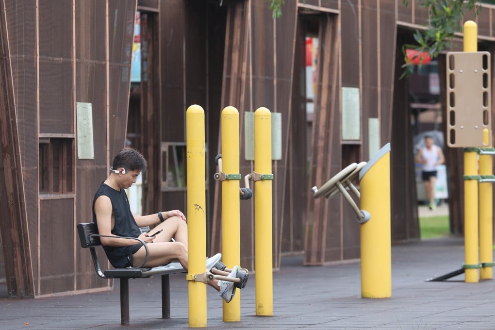 A man checks his phone while using exercise equipment at the Kwun Tong promenade in July 2024. Photo: Edmond So