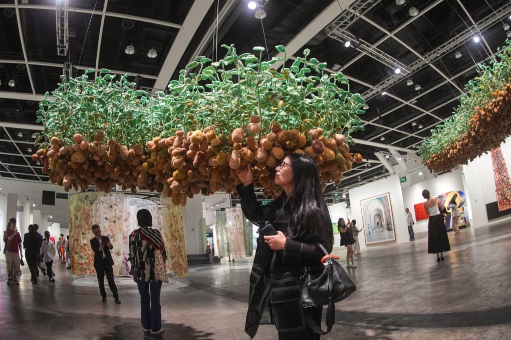 A visitor poses for a photo with Hu Yinping’s Potatoes Grow on Trees at the preview of Art Basel at the Hong Kong Convention and Exhibition Centre in Wan Chai on March 25. Photo: Eugene Lee