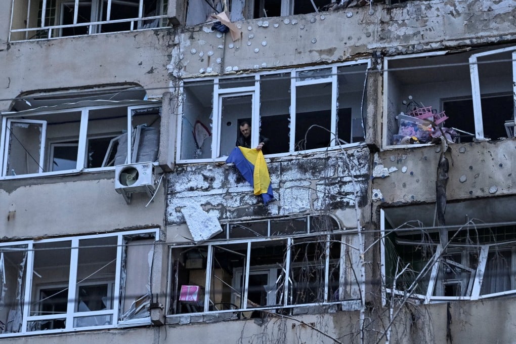 A resident of Lviv hangs the Ukrainian national flag on his balcony after the building was hit by a Russian drone. Photo: Reuters