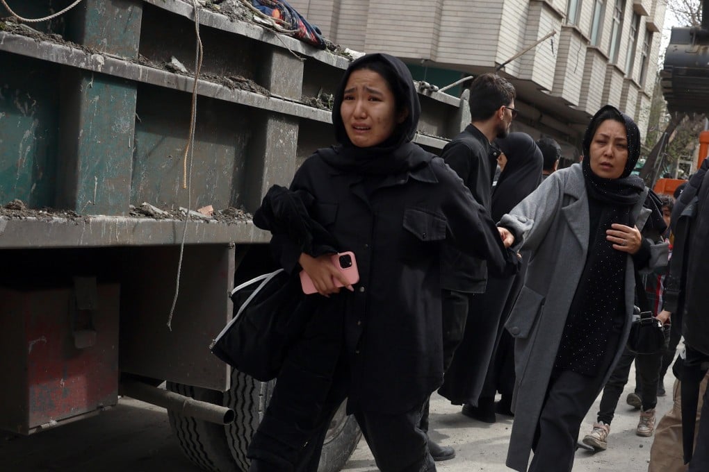 People hurry past damaged residential buildings in southern Tehran, on March 27. Photo: EPA