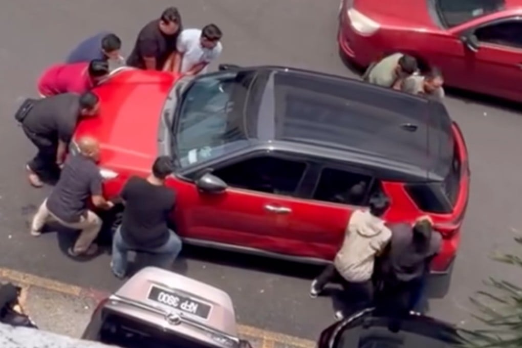 Men lift a car that is blocking a driver from reversing out. Photo: Threads/wnasyh