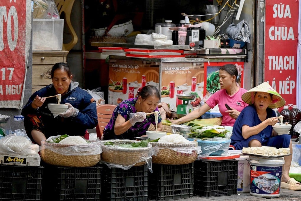 Women sit and eat rice noodles on the sidewalk in Hanoi, Vietnam, on April 14. Photo: AFP