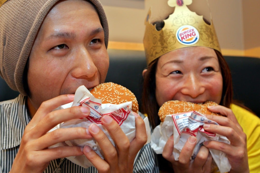 Two customers bite Burger King’s Whopper hamburgers after the chain’s first Tokyo store officially opened in Shinjuku, Tokyo, in 2007. Photo: AP