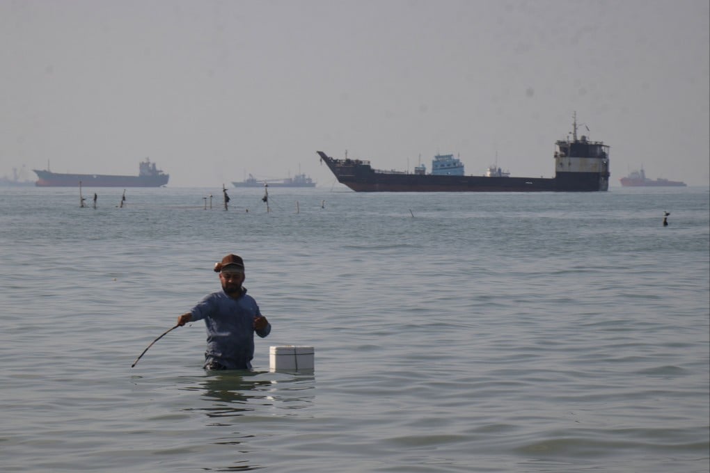 A man stands in the water as ships line the horizon in the Strait of Hormuz in April. Poto: ISNA via AP