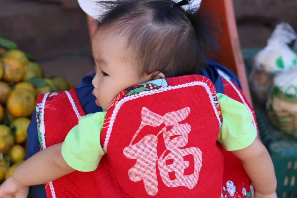 A baby is carried in a back sling adorned with the Chinese character meaning “fortune” in Ban Arunothai, Thailand. Photo: Thomas Bird