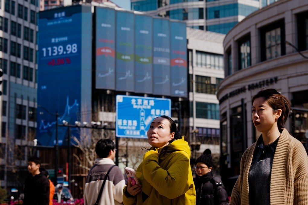 People cross the street beneath a large screen showing the latest stock exchange data in Shanghai. Photo: EPA