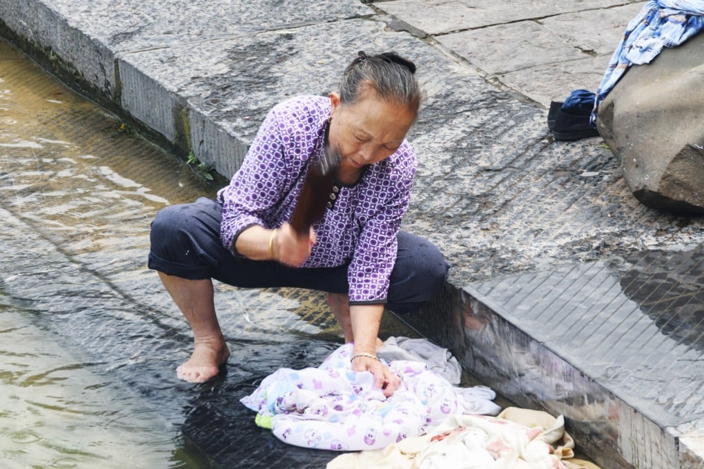 An elderly woman washes clothes the old-fashioned way in a river in Fenghuang Ancient Town in China’s Hunan province. Before the advent of washing machines and chemical detergents, laundry was a labour-intensive affair shaped by local environments and available materials, with clothes typically washed in rivers or streams. Photo: Shutterstock