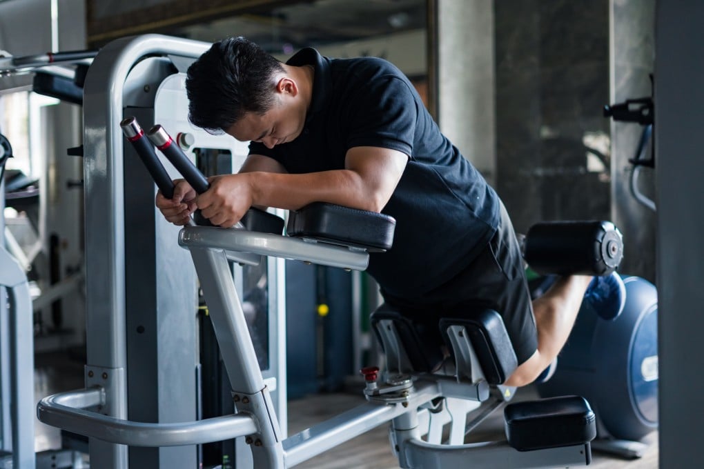 An Asian individual diligently performs a leg exercise using a machine to enhance strength and fitness, demonstrating commitment to health in a contemporary gym setting. Photo: Shutterstock