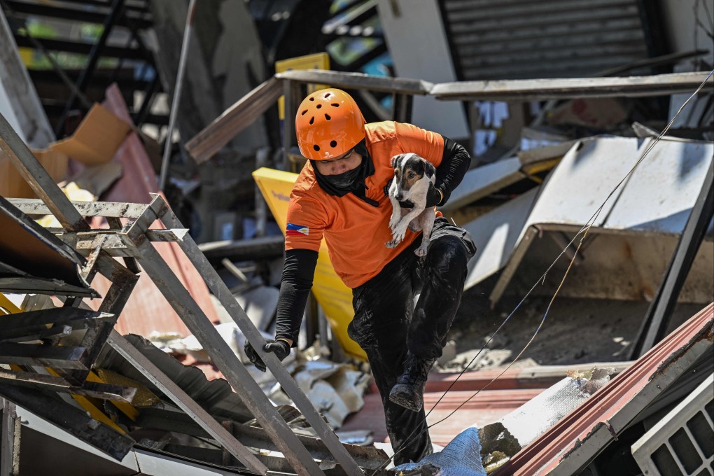 A responder carries a rescue dog while conducting search and rescue operations in a collapsed building after the Mindanao 7.8 magnitude earthquake, in General Santos City on Tuesday. Photo: AFP