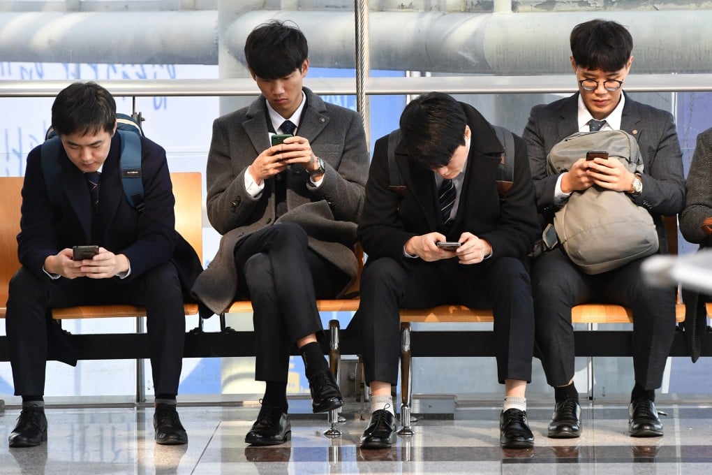 Men look at their smartphones while waiting in Seoul. Photo: AFP