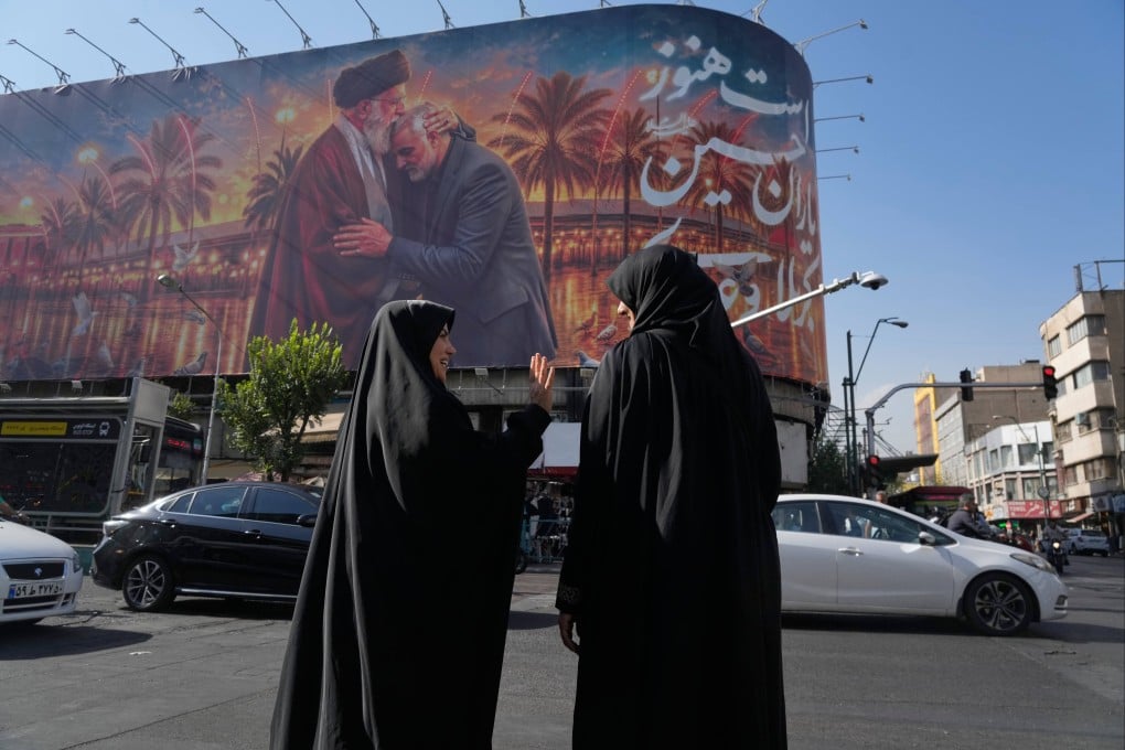 Women talk in front of a banner depicting slain Iranian Supreme Leader Ayatollah Ali Khamenei kissing head of the late commander of Iran’s Revolutionary Guard expeditionary Quds Force, General Qassem Soleimani, in downtown Tehran on Monday. Photo: AP