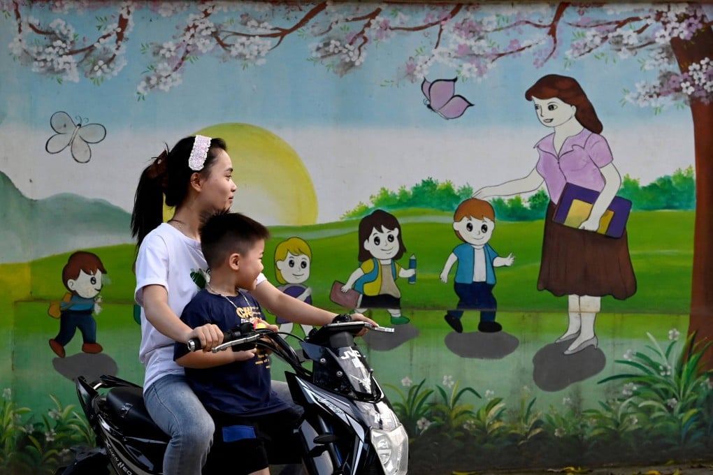 A woman rides an electric motorbike with a child past a mural depicting a teacher welcoming children to school in Hanoi last month. Photo: AFP