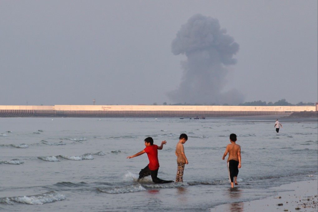 Boys play in the shallow waters of the Strait of Hormuz, as a plume of smoke rises from an explosion in the background, off Bandar Abbas, Iran, on Monday. Photo: ISNA via AP