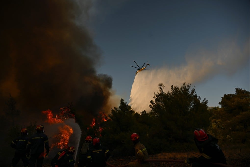 A firefighting helicopter drops water over a smoke-filled forest during a wildfire northwest of Athens, Greece on Sunday. Photo: AP