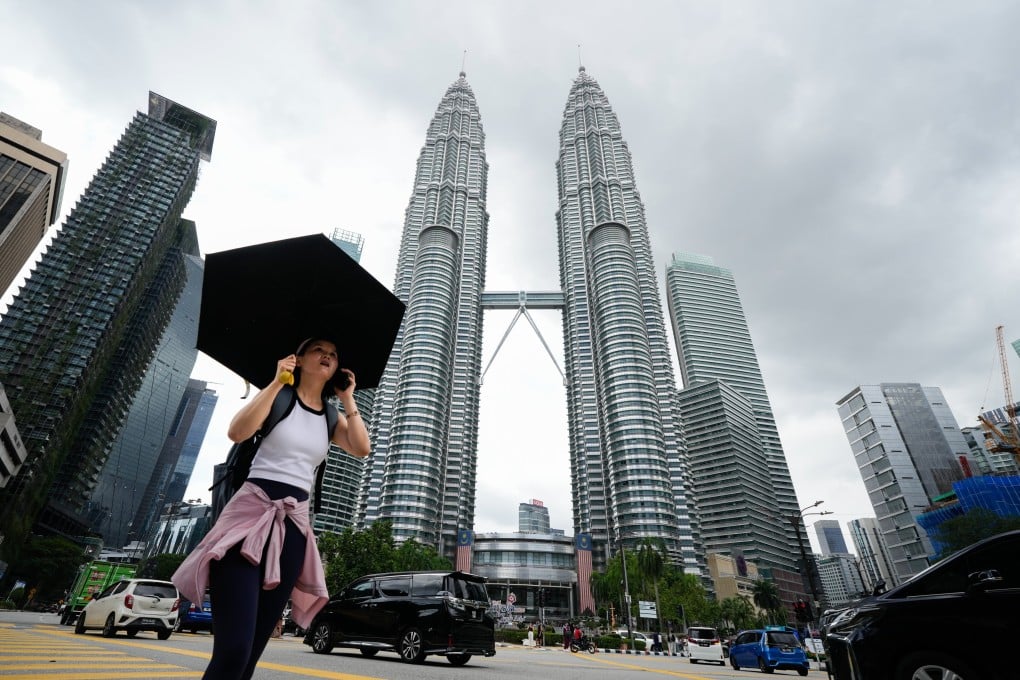 A pedestrian carries an umbrella crosses a street in front of the Petronas Twin Towers in Kuala Lumpur, Malaysia, on Tuesday. Photo: AP