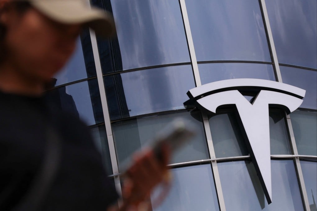 A woman uses her phone as she walks past a Tesla store in Beijing on July 31. Photo: Tingshu Wang