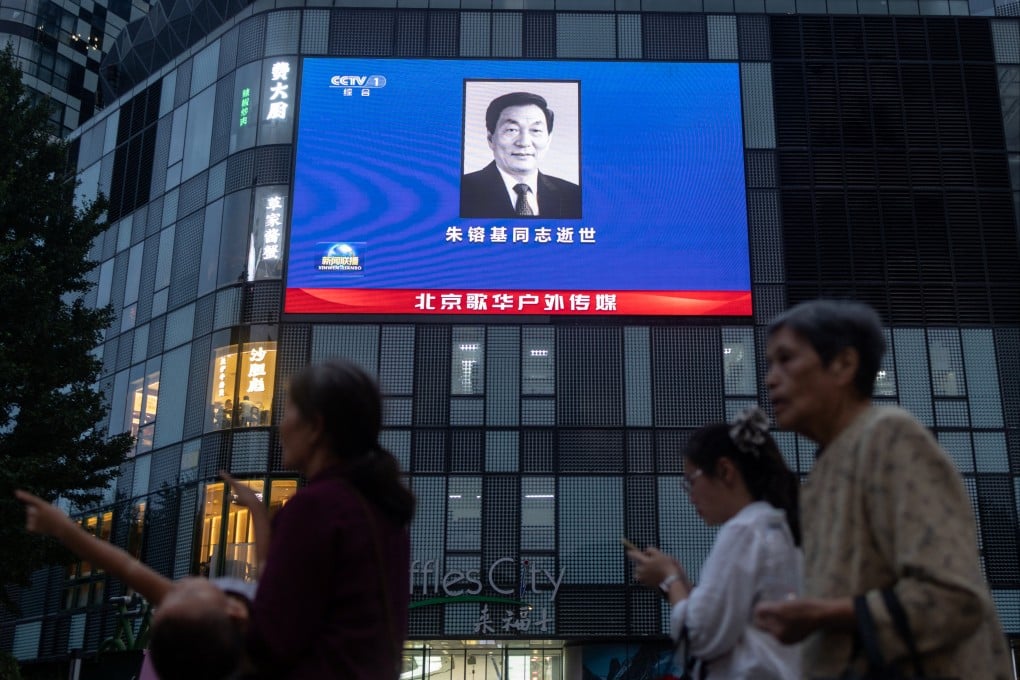 People walk by a shopping mall with a screen showing the news of former Chinese premier Zhu Rongji’s death, in Beijing on August 12. Photo: Reuters