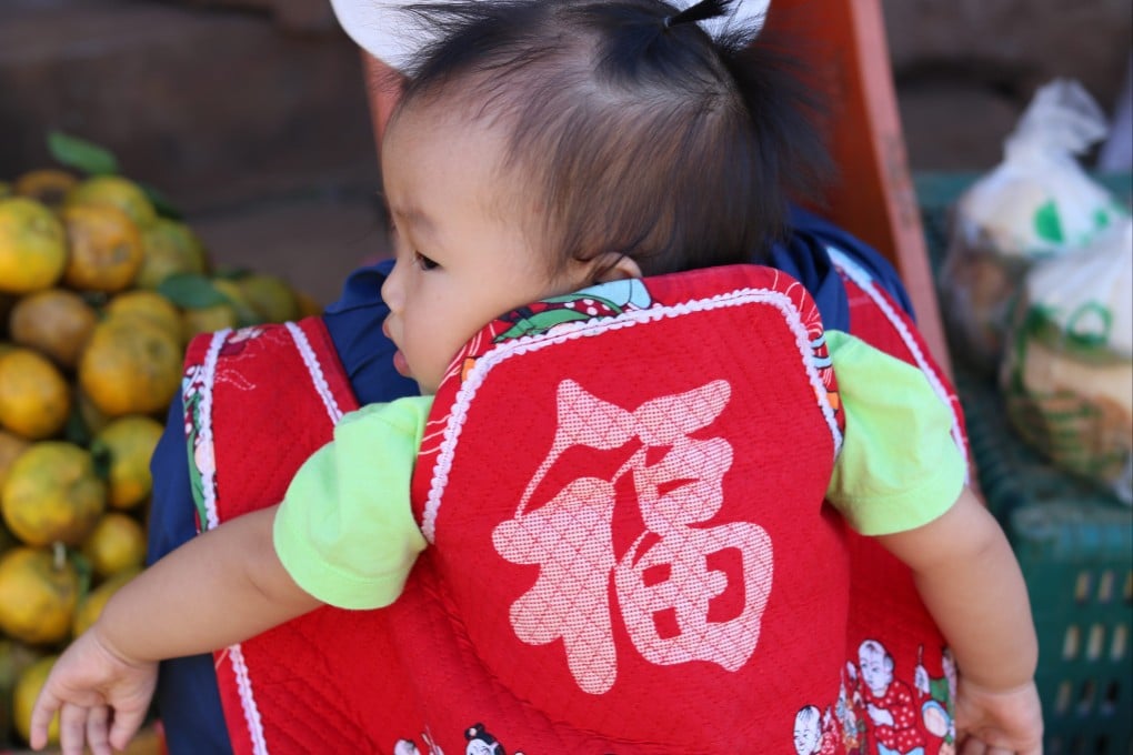 A baby in a back sling adorned with Chinese character meaning “fortune” in Ban Arunothai, Thailand. Photo: Thomas Bird