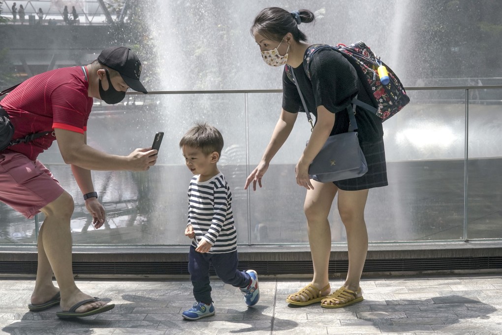 A young child is flanked by his parents in front of the Rain Vortex waterfall inside the Jewel Changi Airport mall in Singapore in June 2021. Photo: EPA-EFE