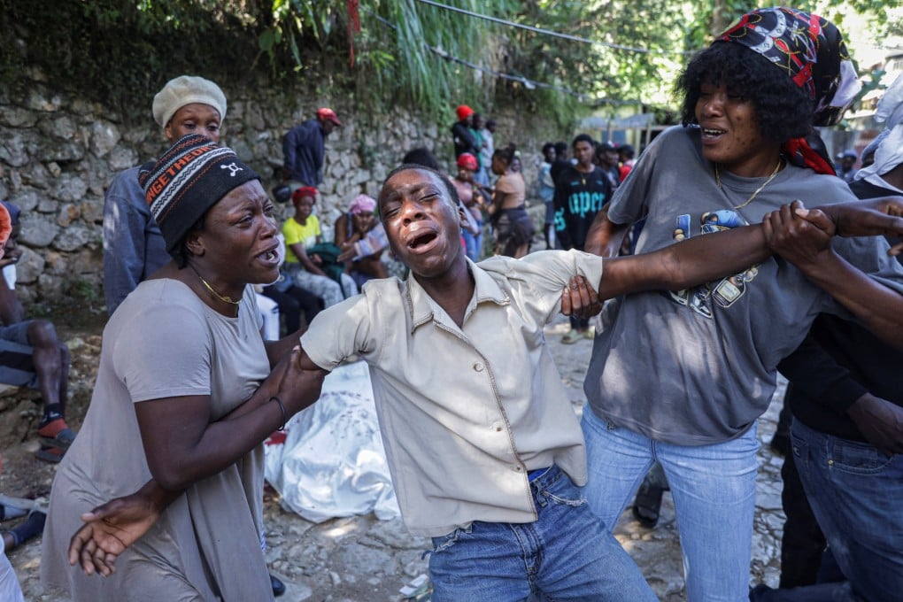A man is comforted as he mourns next to a covered body following an overnight gang attack. Photo: Reuters