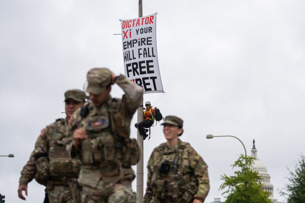 A protester scales a light pole and unfurls a banner to protest the coming state visit by Chinese President Xi Jinping in Washington on Tuesday as members of the National Guard walk by. Photo: AP