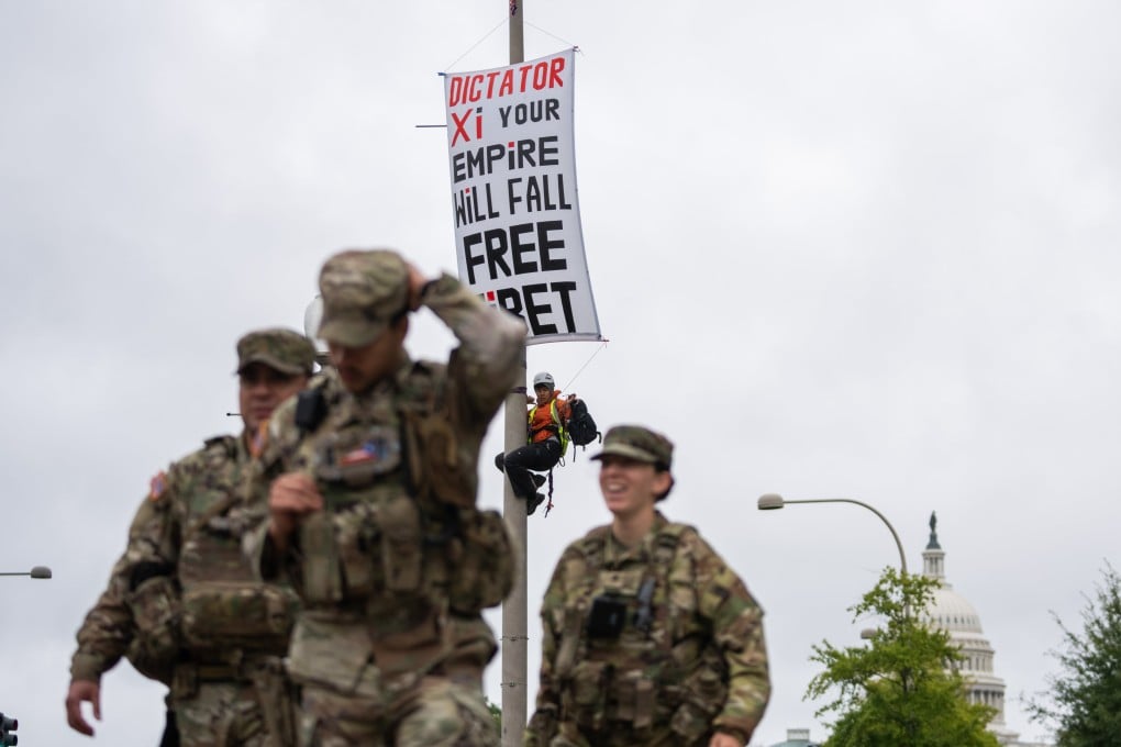 A protester scales a light pole and unfurls a banner to protest the coming state visit by Chinese President Xi Jinping in Washington on Tuesday as members of the National Guard walk by. Photo: AP