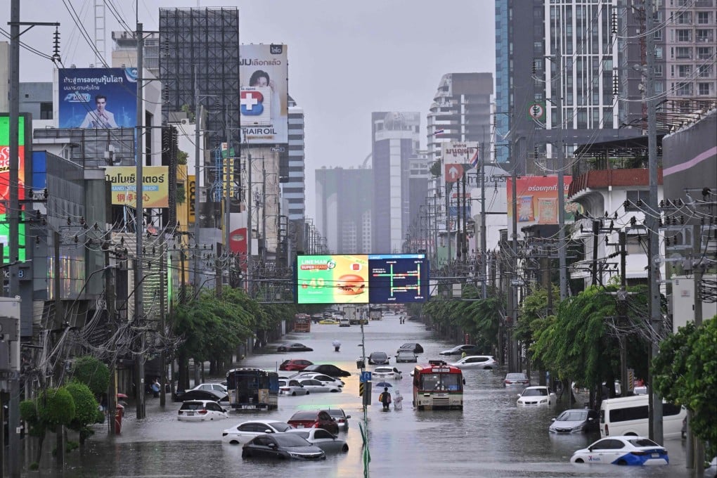 People walk past abandoned vehicles on a flooded Petchaburi Road in Bangkok on Saturday. Photo: AFP
