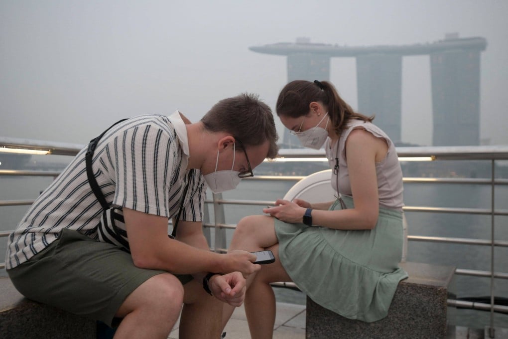 Tourists wearing protective masks sit near Marina Bay Sands in Singapore on Thursday as haze from Indonesian forest fires shrouds the city state. Photo: AFP